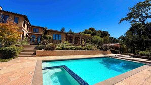 A pool with a tiled edge, a building with a tiled roof, and a clear blue sky.