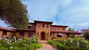 A two-story house with a central entrance, surrounded by well-maintained gardens and a paved walkway.