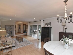 A spacious living room with a sofa, coffee table, and a dining table with a vase of flowers.