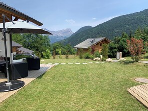 Eine Holzhütte mit Satteldach, umgeben von einer gepflegten Rasenfläche und einem Blick auf die Berge.