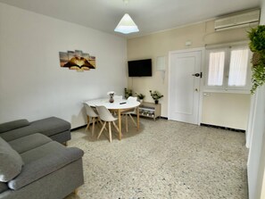 A living room with a grey sofa set, a dining table with chairs, a flat-screen TV mounted on the wall, and a door with a window. - Sand and Sun in Staycare (Chipiona)