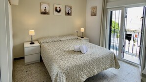 Un dormitorio con una cama, dos mesitas de noche con lámparas, una planta colgada en la pared y obras de arte.