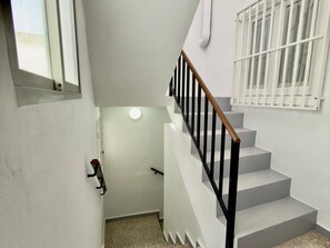 A staircase with white steps and black railings, leading to a landing with a door and a window. - Sand and Sun in Staycare (Chipiona)