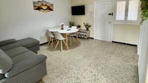 Un espacio habitable pequeño con sofá, una mesa de comedor con sillas, un televisor montado en la pared y una puerta con ventanas.