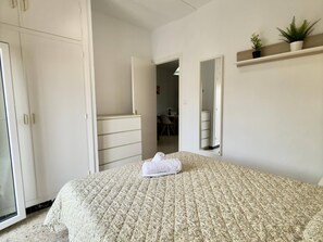 A bedroom with a bed, a wardrobe, a mirror, and a small plant on a shelf. - Sand and Sun in Staycare (Chipiona)