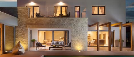 A modern two-story house with a swimming pool, outdoor seating, and a stone facade.