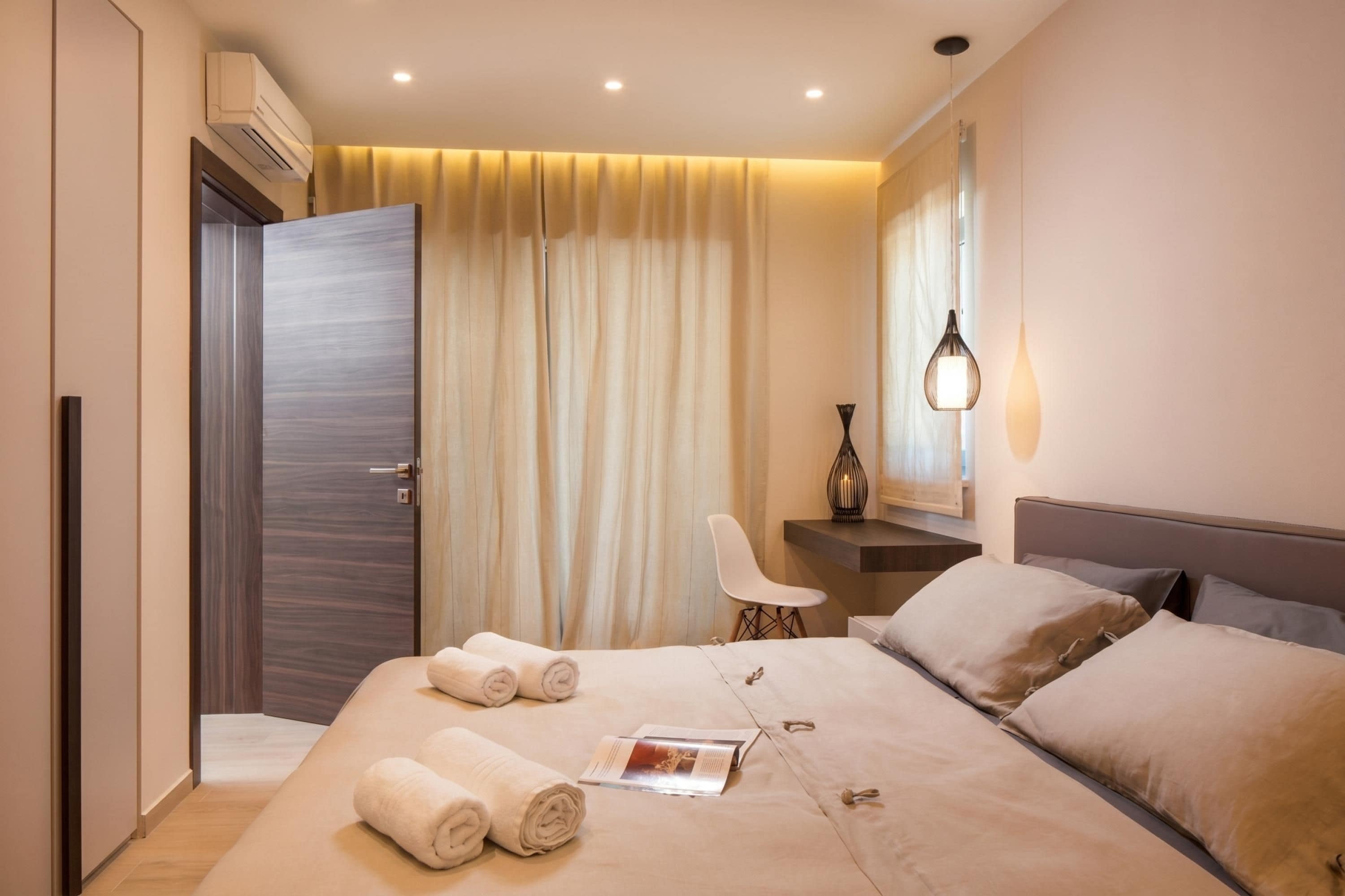 A modern hotel room with a large bed, a desk, a chair, and a mirror.