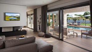 Uma sala de estar moderna com uma televisão grande, assentos confortáveis e uma porta de vidro que dá para uma área de piscina.
