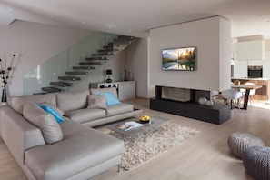 A modern living room with a sofa, coffee table, fireplace, and staircase. - Villa Royal Green (Rasa)