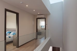 A modern interior with a glass railing, a bed with a headboard, and an air conditioning unit on the wall. - Villa Royal Green (Rasa)