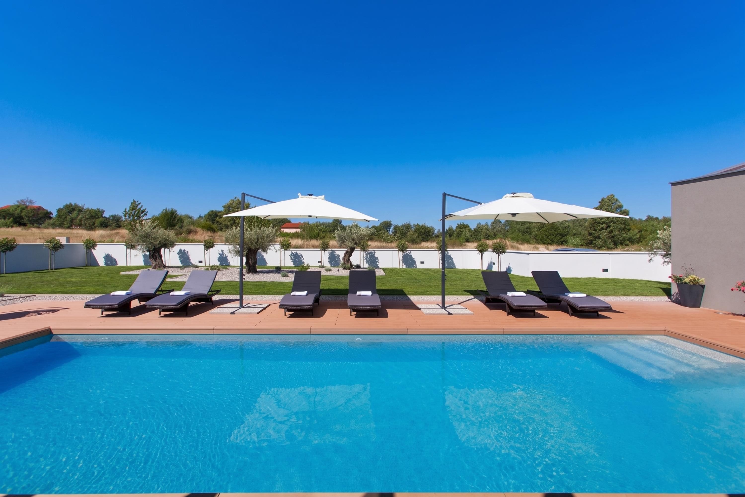 A swimming pool with lounge chairs and umbrellas, surrounded by a landscaped garden and a building.
