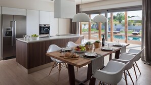 Cozinha moderna com ilha central, área de refeições com cadeiras brancas e vista para uma piscina.