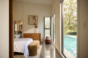 A bedroom with a bed, a wooden headboard, a large window, and a view of a swimming pool.