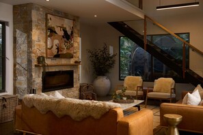 A modern living room with a stone fireplace, a flat-screen TV, comfortable seating, and a staircase with glass railings.