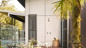 A modern outdoor area with a glass-enclosed pool, a wooden deck, and a door leading to a covered space. - The Pavilion, Wamberal (Wamberal)