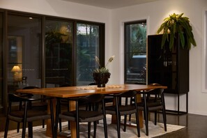 A dining area with a wooden table, black chairs, a potted plant, and a black bookshelf.