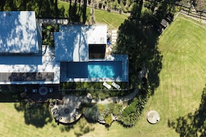 An aerial view of a modern house with a swimming pool, a deck, and a well-maintained lawn.