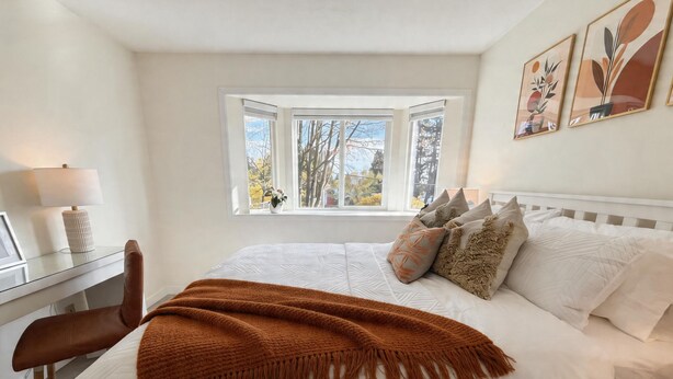 A bedroom with a bed, a desk, a chair, a window, and wall art.