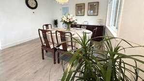 A dining room with a round table, chairs, a chandelier, a clock, framed artwork, and a window.