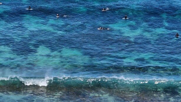 Une plage avec une eau bleu clair, des vagues et des rochers.