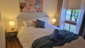 Une chambre d’hôtel avec un lit, deux lampes de chevet, une table de nuit, une fenêtre avec des rideaux et un tableau au mur.