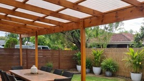 Une terrasse couverte avec une table et des chaises en bois, entourée de plantes en pot.