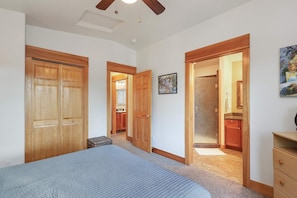 A bedroom with a bed, a ceiling fan, wooden doors, a hallway, and a bathroom.