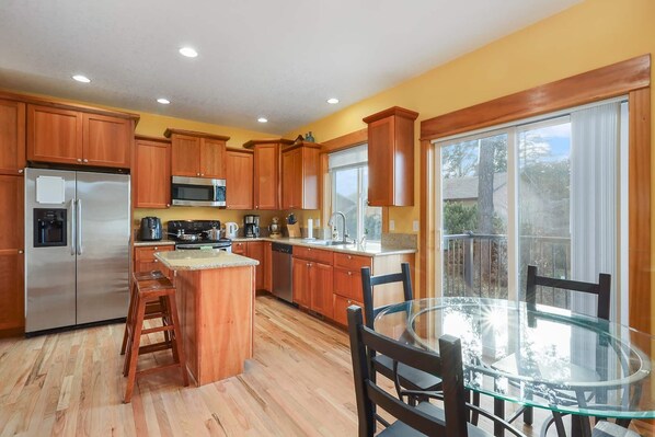 A kitchen with wooden cabinets, stainless steel appliances, a glass island, and a dining area with a glass table and chairs.