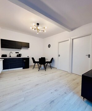A modern kitchen with dark cabinets, a dining table with four chairs, and a ceiling light fixture.