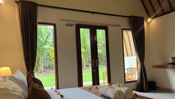 Habitación de hotel con cama, cortinas, ventana con vistas a zonas verdes, una mesita con hervidor y una silla.