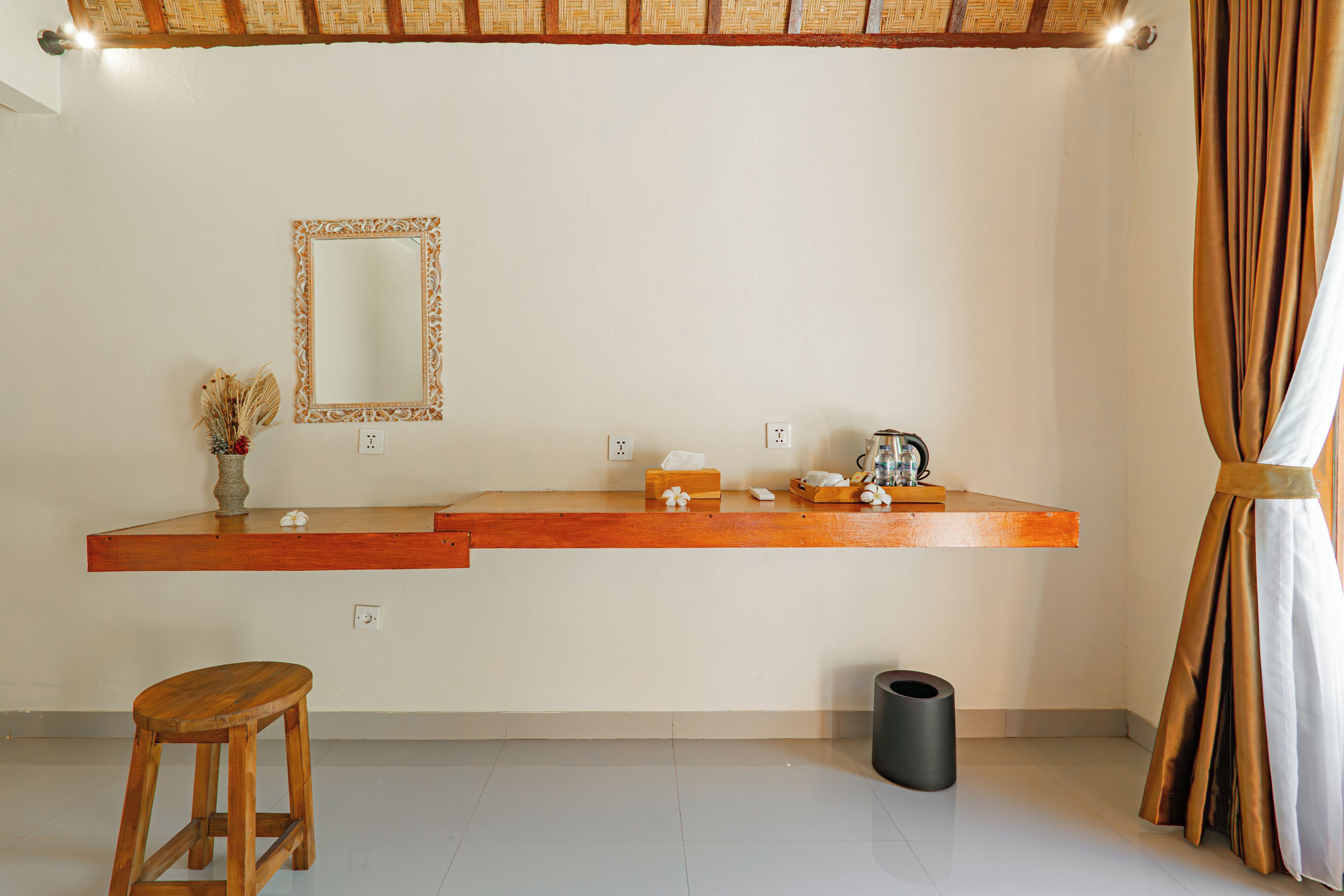 Una habitación con un banco de madera, un espejo, un estante con artículos de tocador y un cubo de basura.