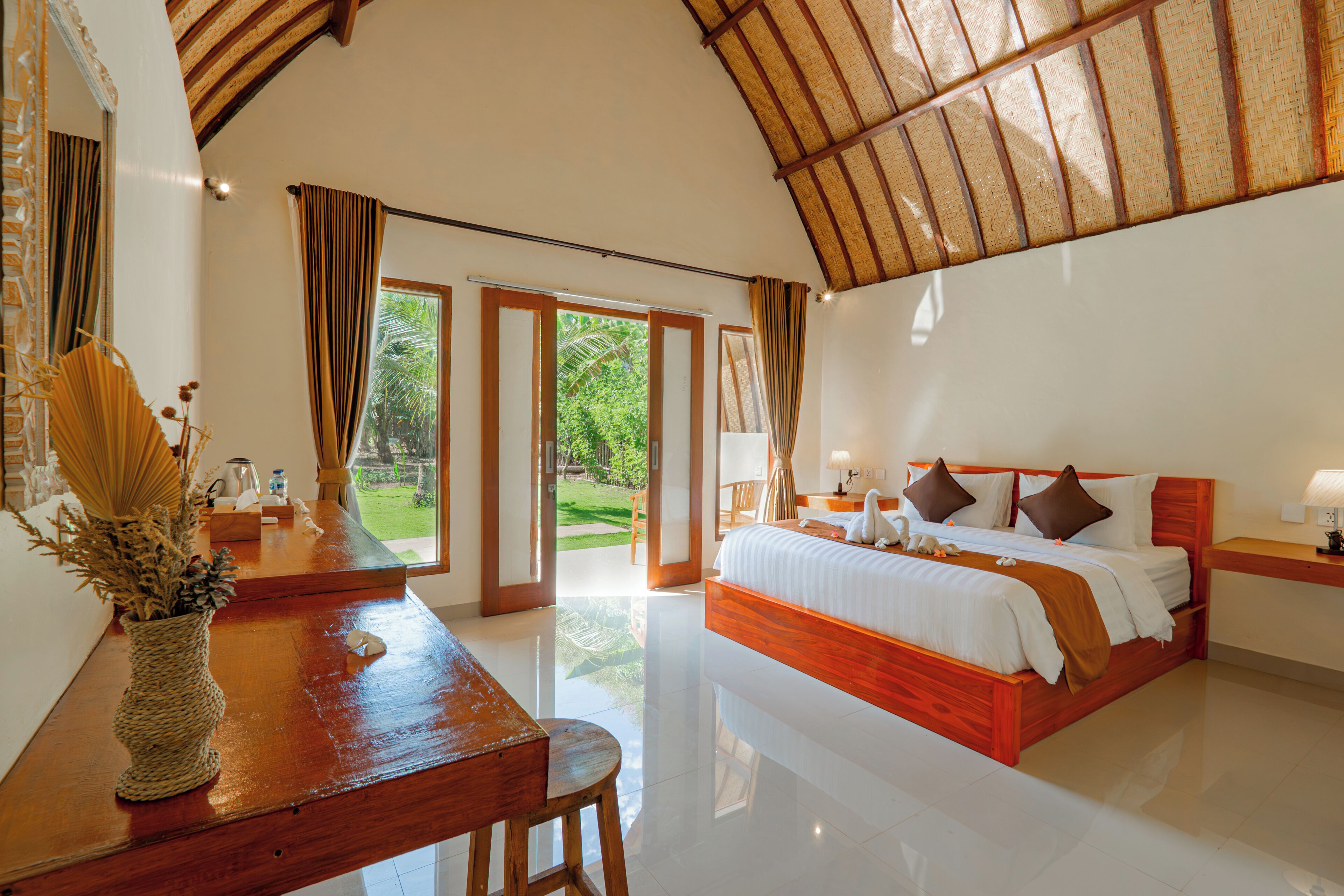 A bedroom with a large bed, a wooden desk, and a view of the outdoors.