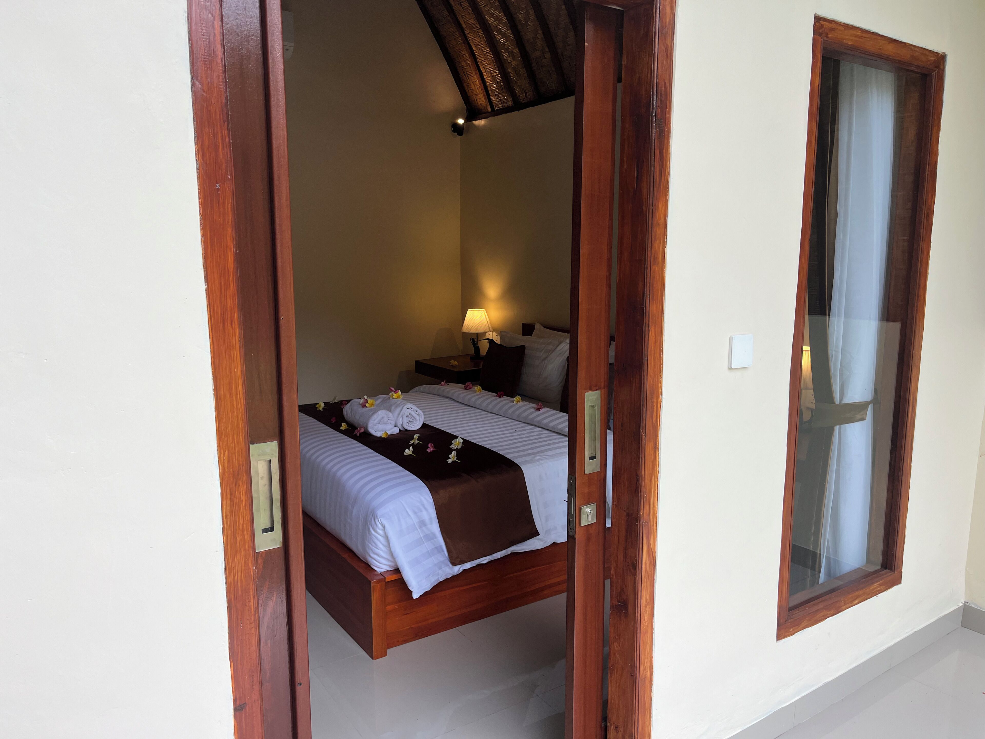 A room with a bed, a nightstand, a lamp, and a window.