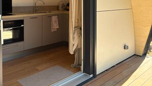 Uma cozinha compacta com pia, fogão e forno, uma luminária pendente e uma porta que dá para um cômodo adjacente.