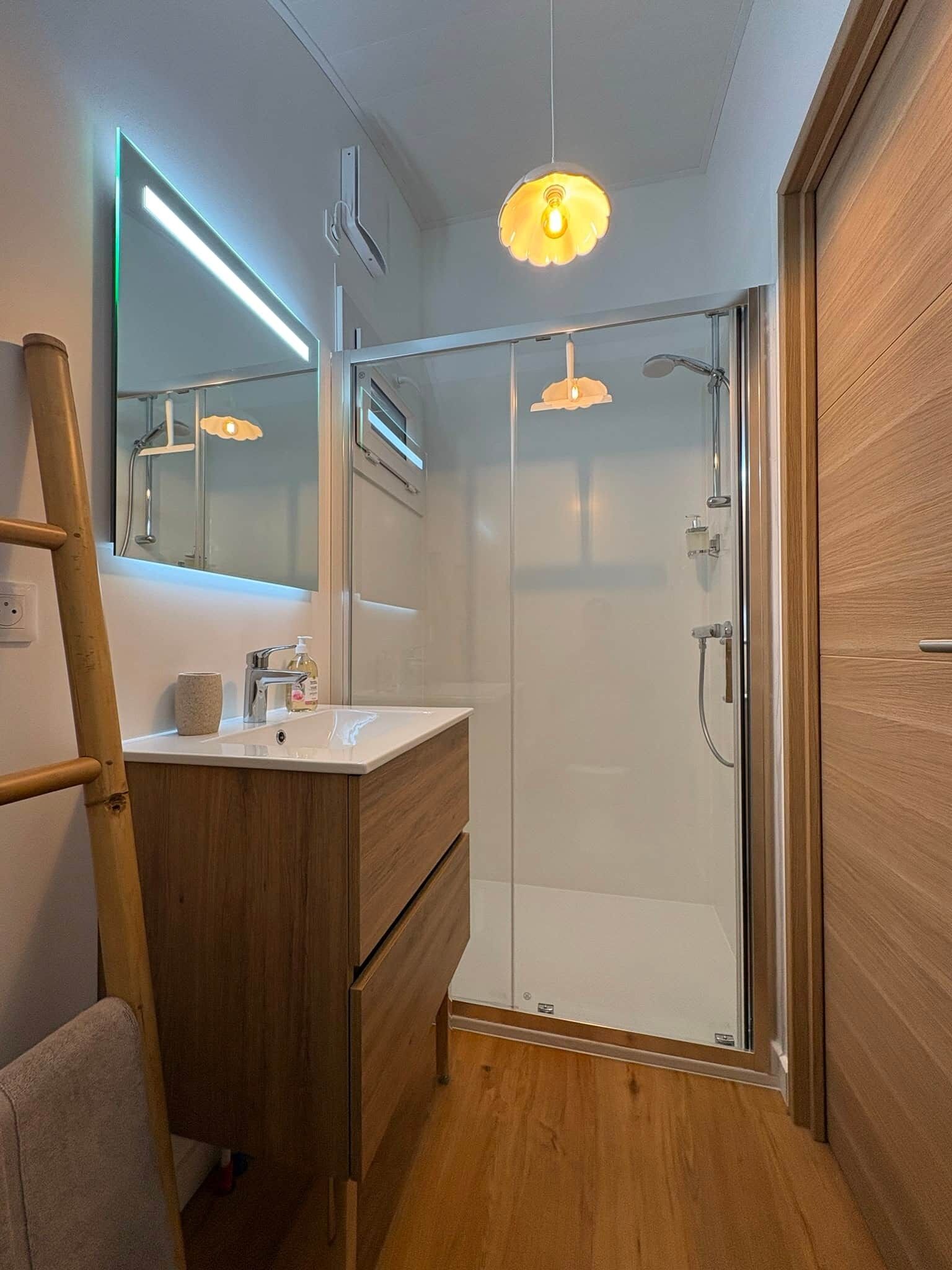 A modern bathroom with a glass shower enclosure, a wooden vanity with a mirror, and a pendant light.