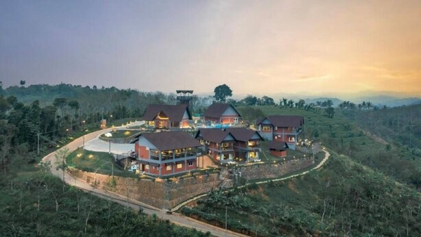 A cluster of red-roofed buildings with a swimming pool, surrounded by lush greenery and hills.