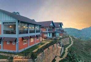 Un hôtel à plusieurs étages doté de balcons, d’un mur de soutènement en pierre et d’un sentier menant vers le haut d’une colline.