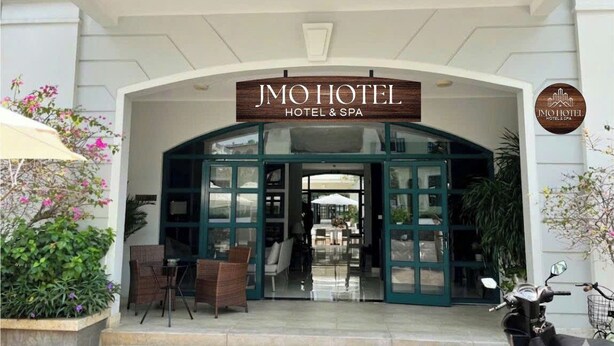 The entrance to JMO Hotel & Spa with a clear glass facade, a sign above the entrance, and outdoor seating. - JMO Boutique Hotel & Spa Phu Quoc (Phu Quoc)