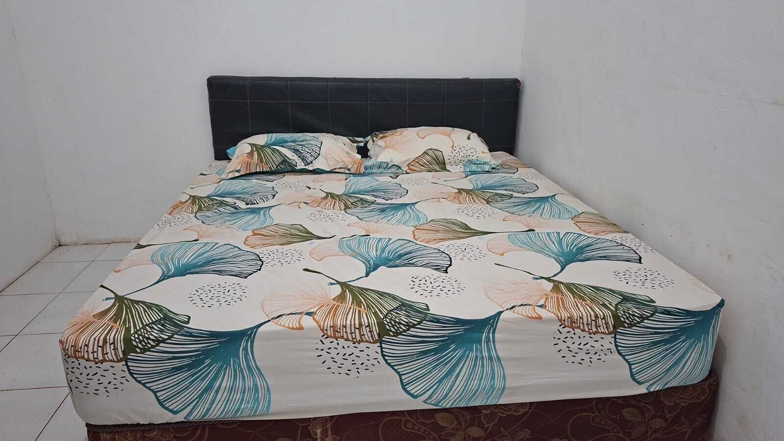 A bed with a floral bedspread, a dark headboard, and a tiled floor.