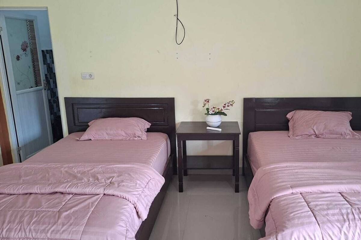 Een kamer met twee bedden, een nachtkastje met een vaas en een deur met een bloemendesign.