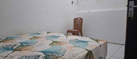 Una habitación pequeña con una cama cubierta por una colcha de estampado floral, una silla de madera y una puerta con manija metálica.