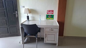 A room with a white desk, a black chair, a lamp, a water bottle, and a sign on the wall.