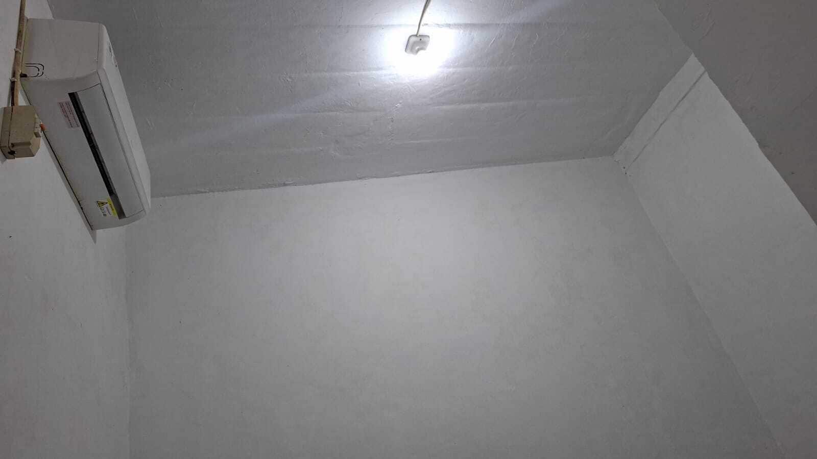 Une pièce aux murs blancs, avec un luminaire au plafond et un appareil de climatisation blanc.