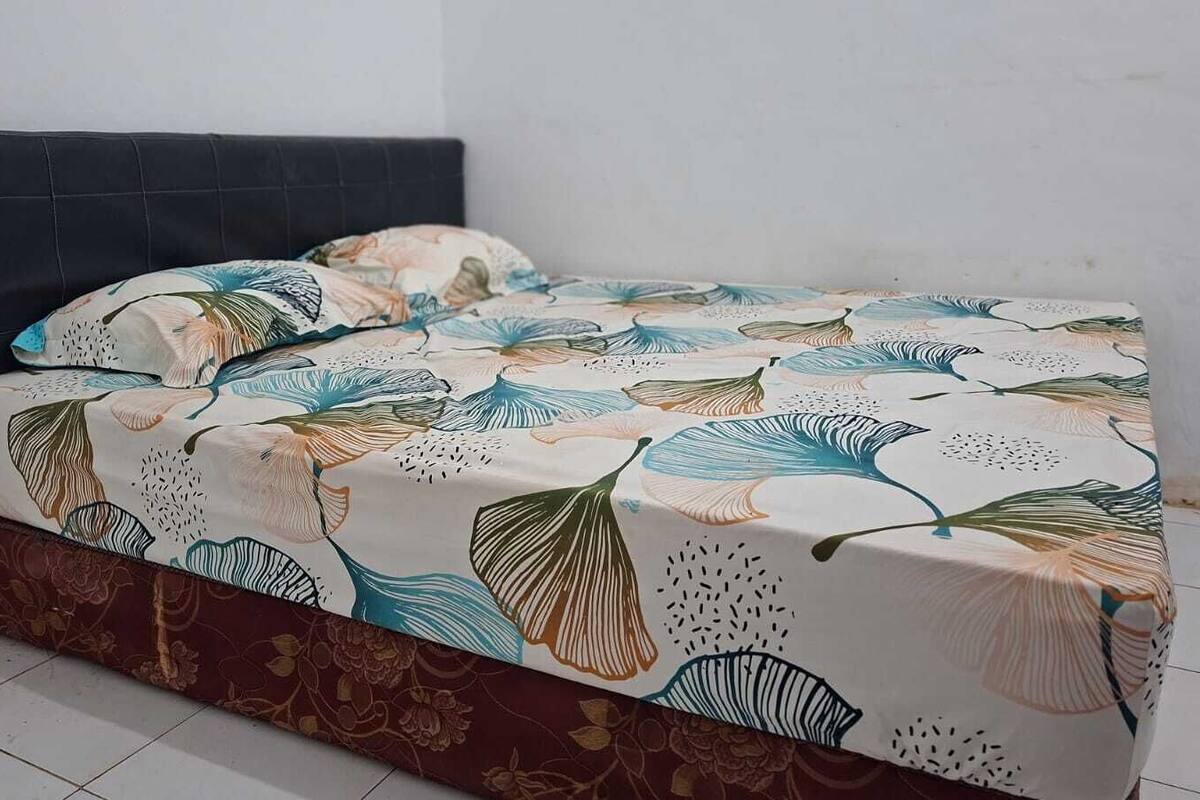 Een bed met een bloemenprint deken, een donker hoofdbord en een bedrok met patroon.