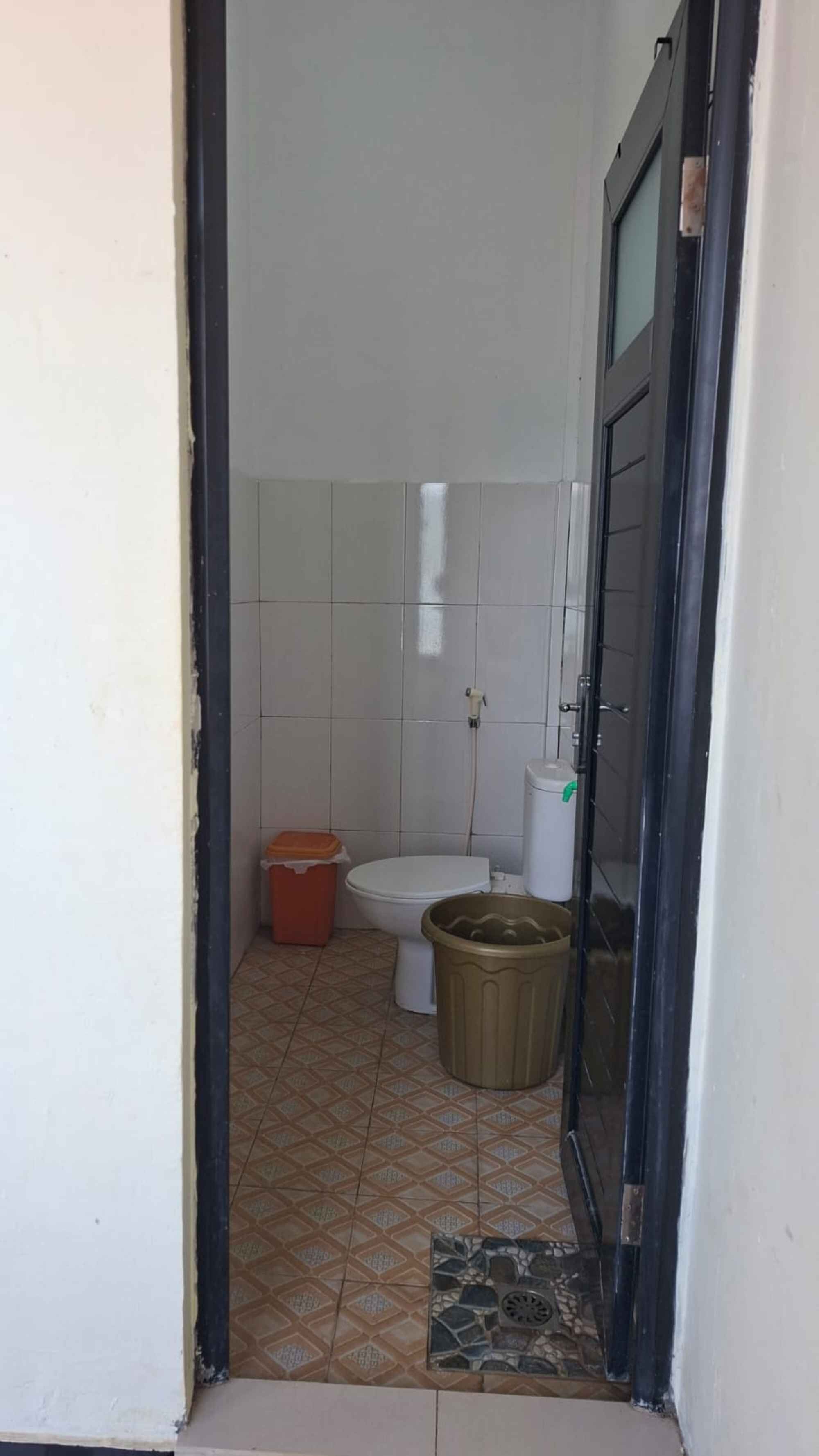 A small, narrow bathroom with a toilet, a trash bin, and a shower area.