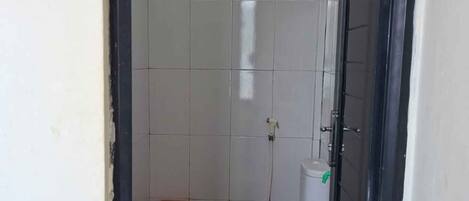 A small, narrow bathroom with a toilet, a trash bin, and a shower area.