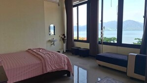 A hotel room with a bed, a sofa, a window with a view of mountains, a sink, and a mirror. - Penginapan Remaja Morowali (Kolonodale)
