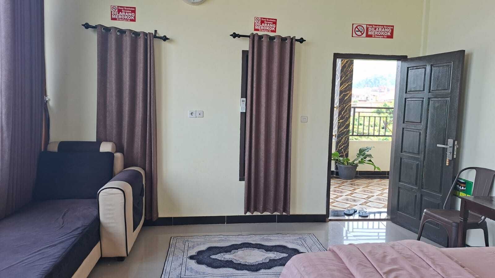 A hotel room with a bed, a sofa, a small table, and a potted plant. There are curtains and a door leading to an outdoor area.
