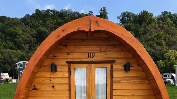 Una cabaña de madera con techo semicircular, número 119, con dos sillas en una terraza de madera.