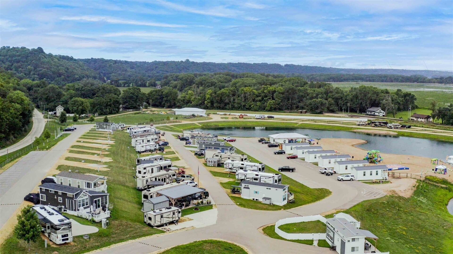 Un camping con vehículos recreativos y casas móviles, un lago y una carretera que serpentea por la zona.